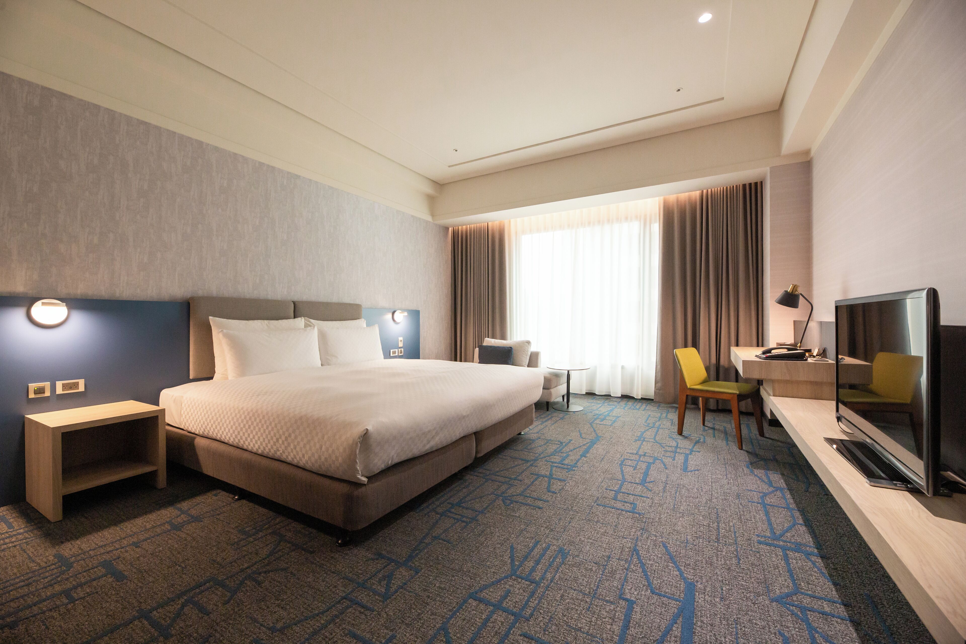 A hotel room with a large bed, a desk with a chair, a TV, and a small table.