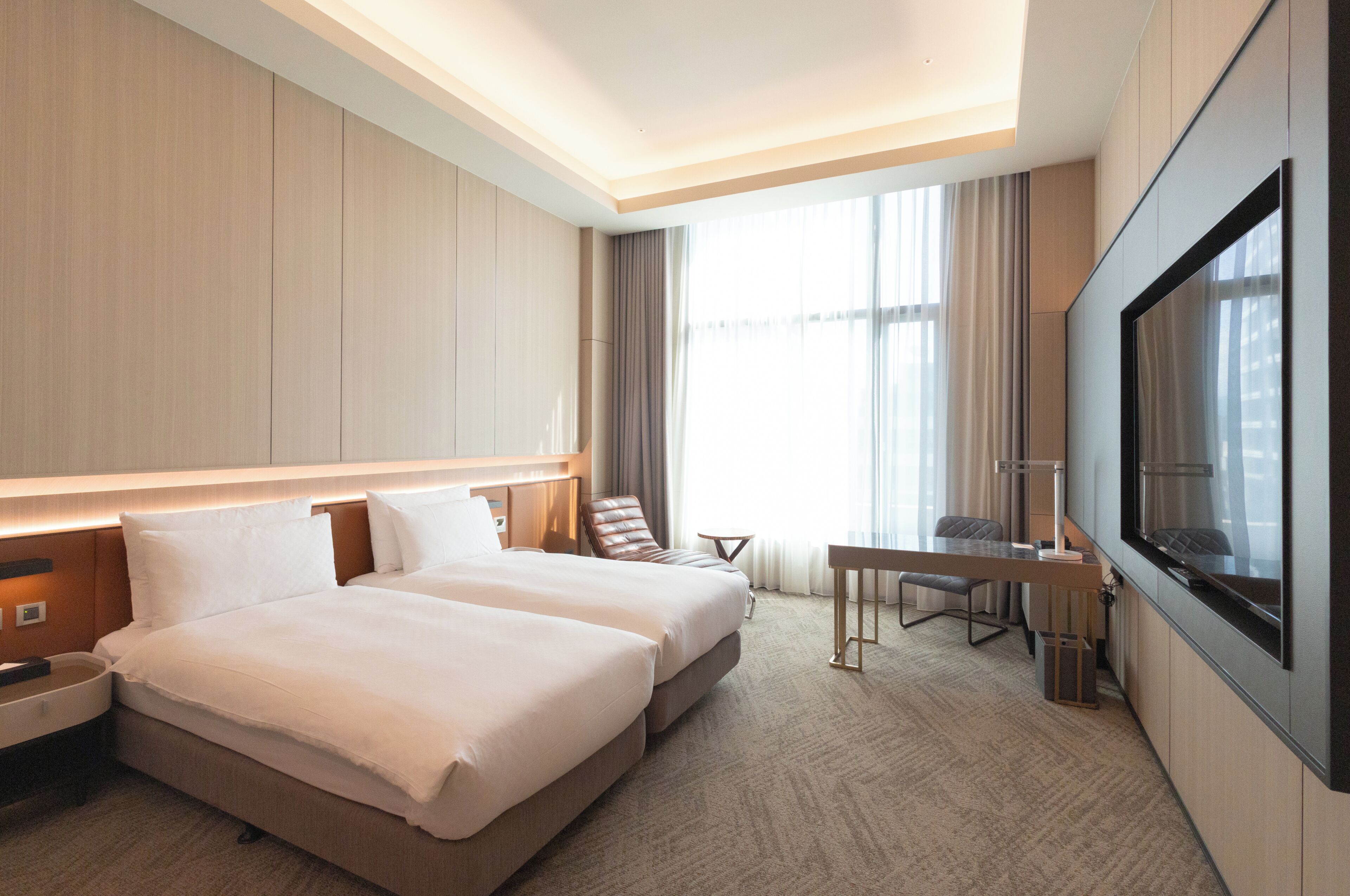 Une chambre d’hôtel avec deux lits, un bureau, une télévision et une grande fenêtre.