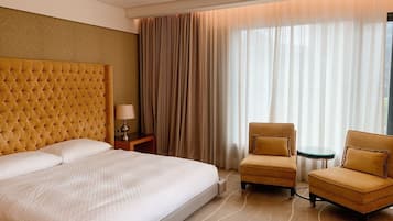 Una habitación de hotel con una cama grande, dos sillones, una mesita y una lámpara.