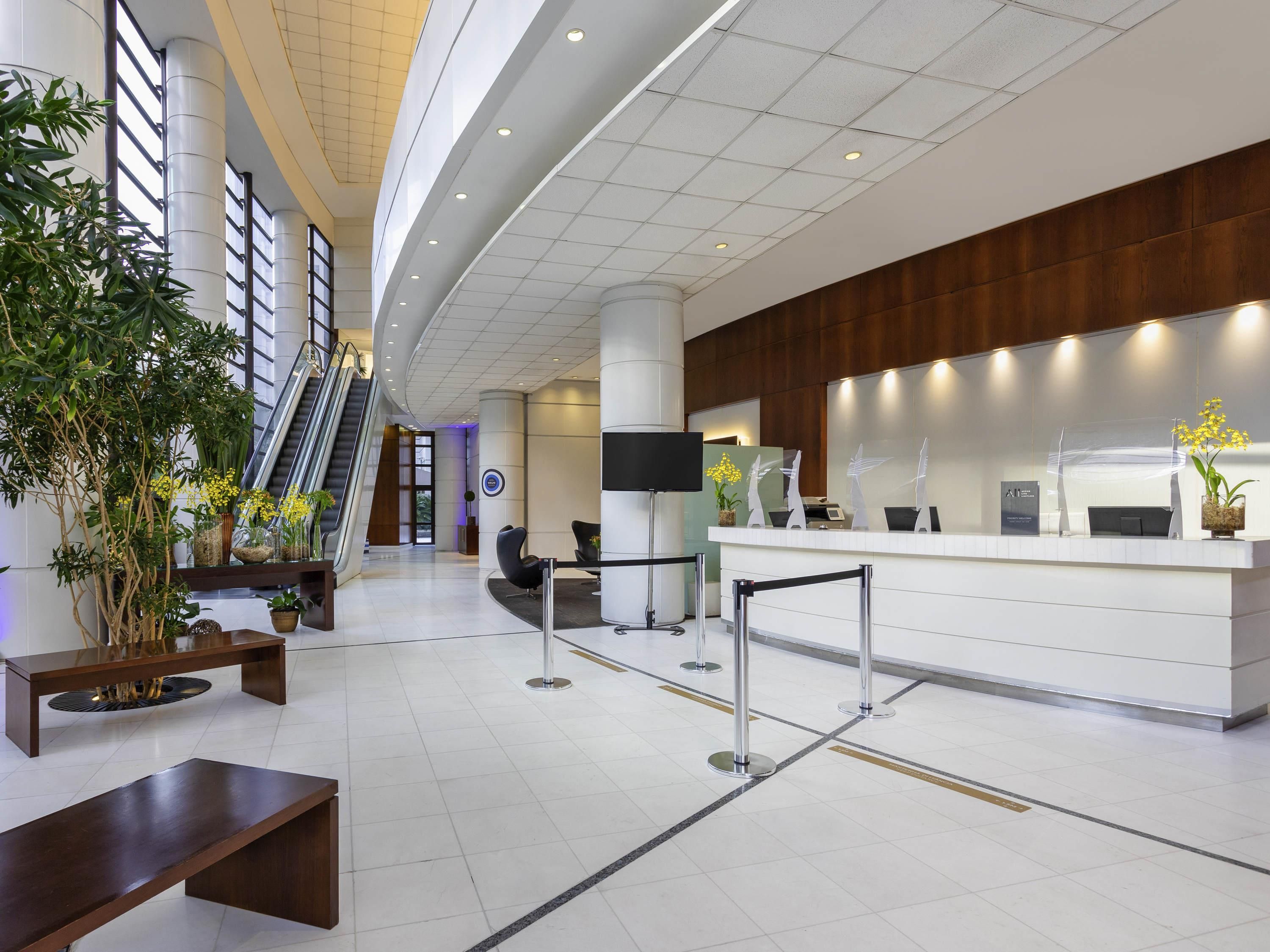 A modern hotel lobby with a reception desk, seating area, and an escalator.
