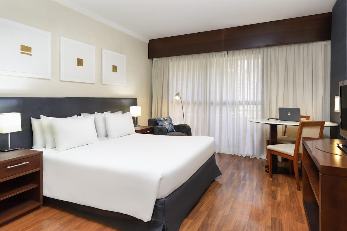 A hotel room with a large bed, a desk with a laptop, a chair, and a TV.