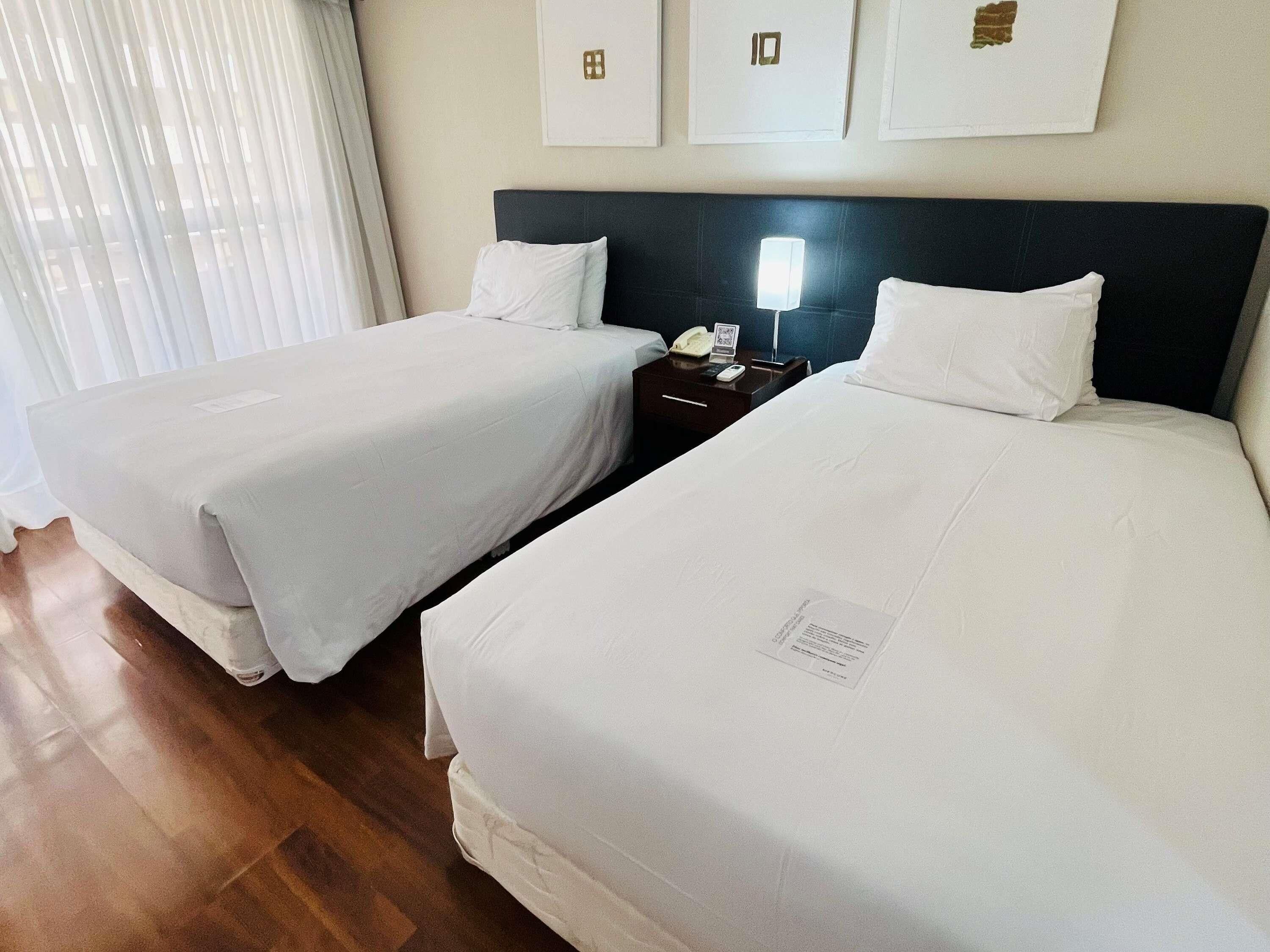 Habitación de hotel con dos camas, una mesita de noche con lámpara y un teléfono en la pared.