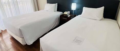 Habitación de hotel con dos camas, una mesita de noche con lámpara y un teléfono en la pared.