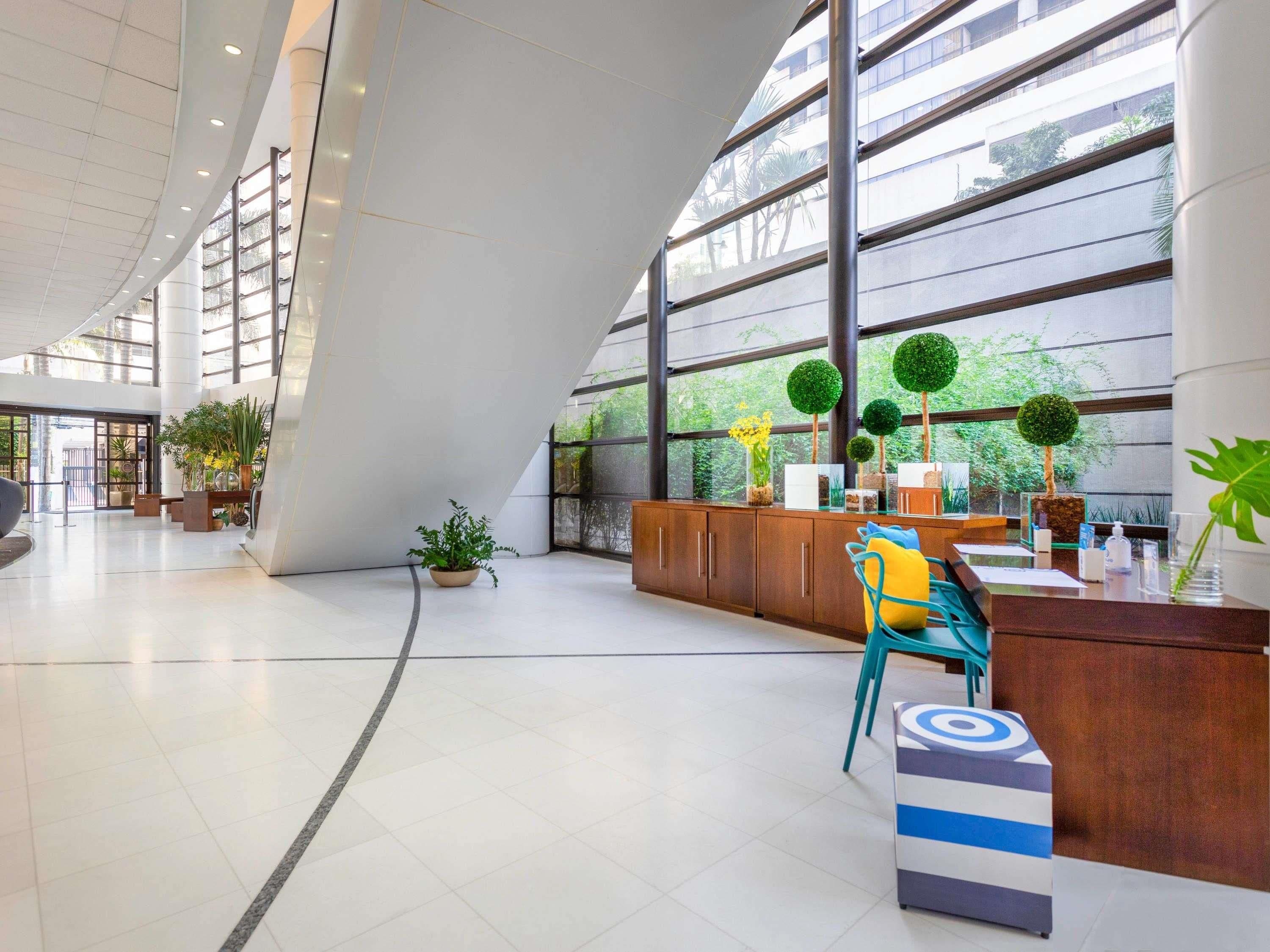 Um hall amplo com balcão de recepção, área de estar e grandes janelas com vista para o verde.