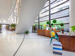 Un vestíbulo amplio con recepción, zona de estar y ventanas grandes que ofrecen vistas a zonas verdes.
