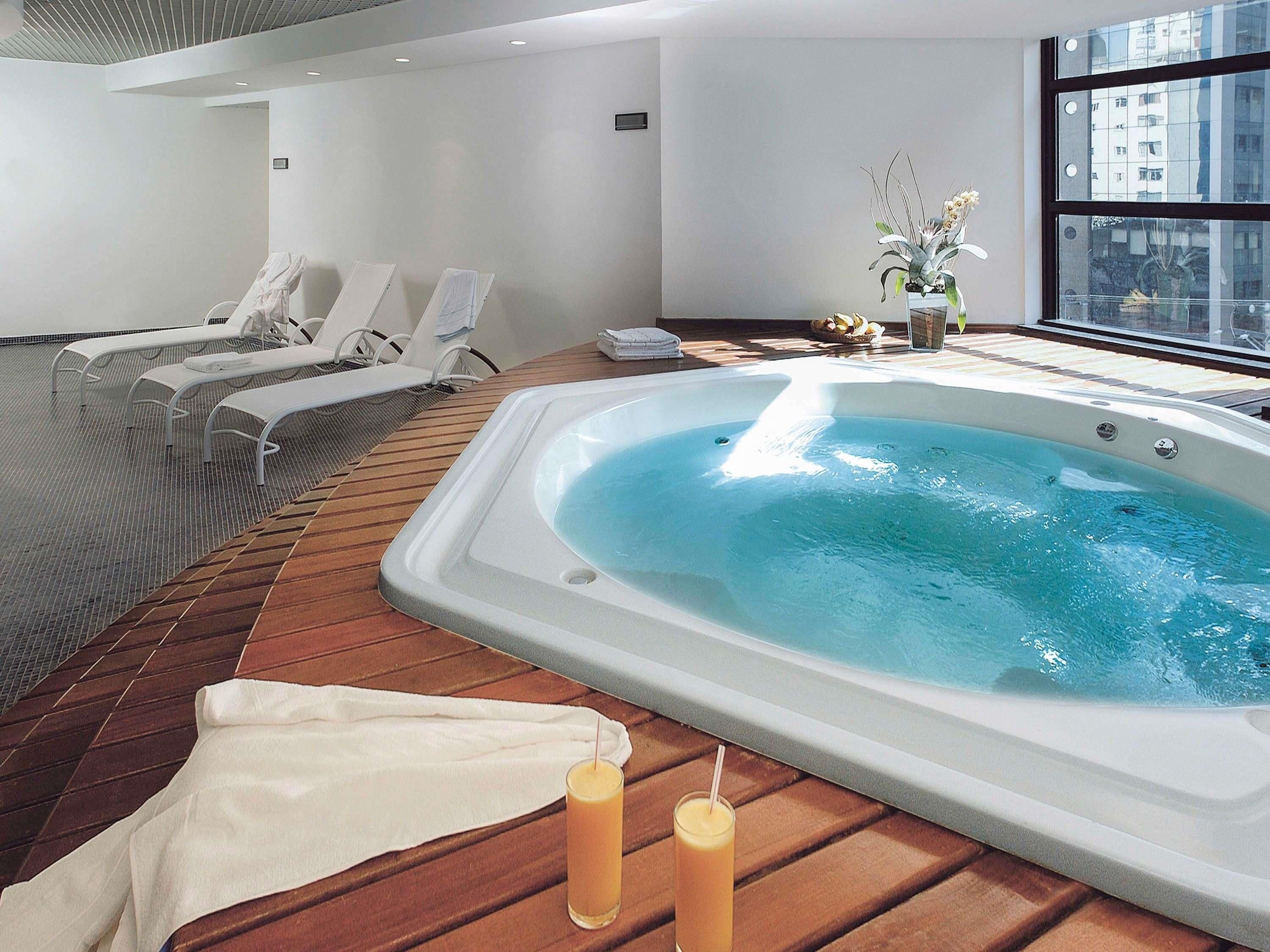 A modern indoor pool area with a hot tub, lounge chairs, and a wooden deck.
