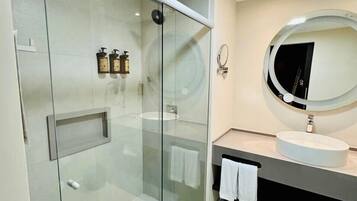 Uma casa de banho moderna com cabine de duche em vidro, espelho redondo e lavatório branco.