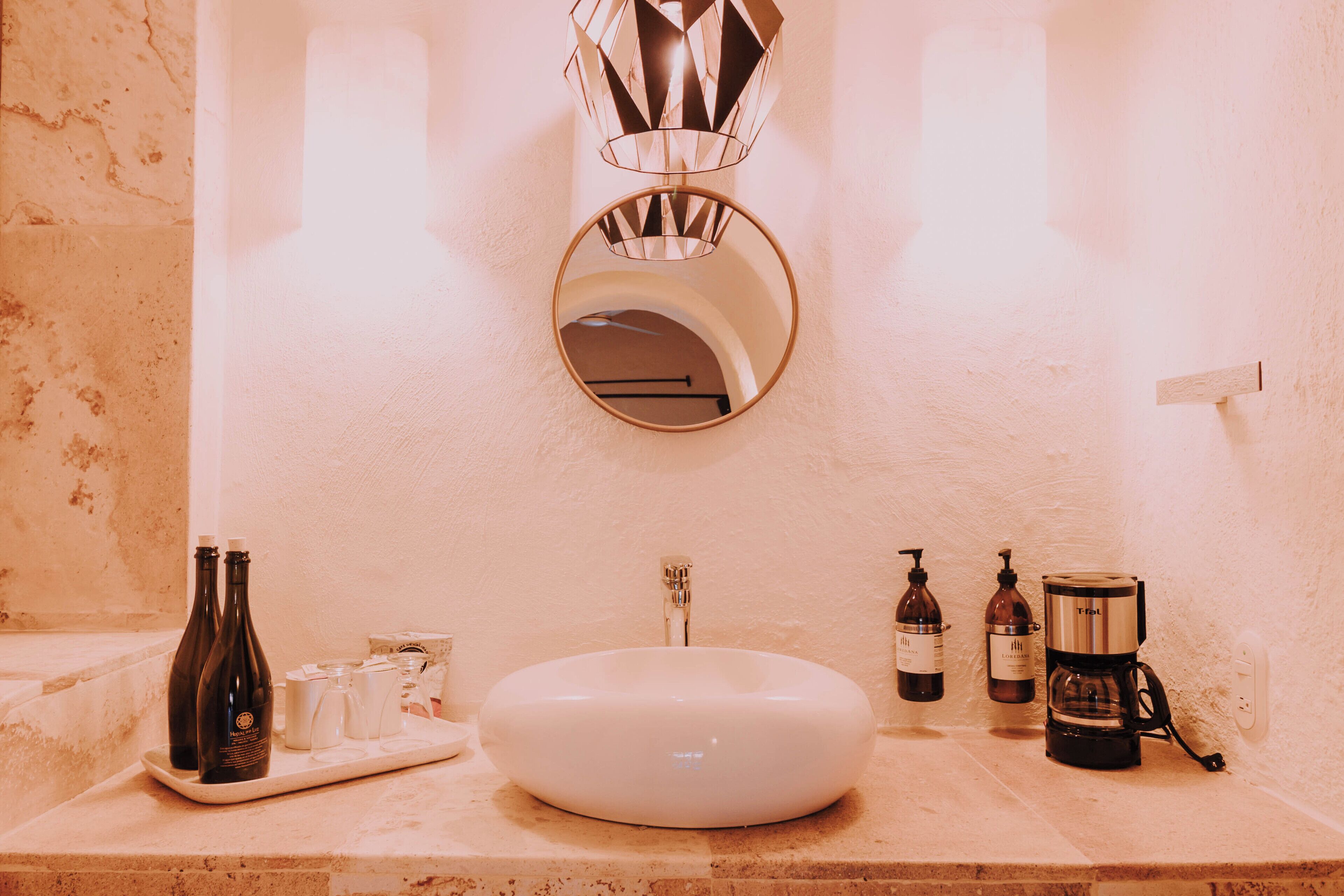 Un baño con lavamanos blanco, espejo, toallero y cafetera.