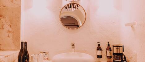 Un baño con lavamanos blanco, espejo, toallero y cafetera.