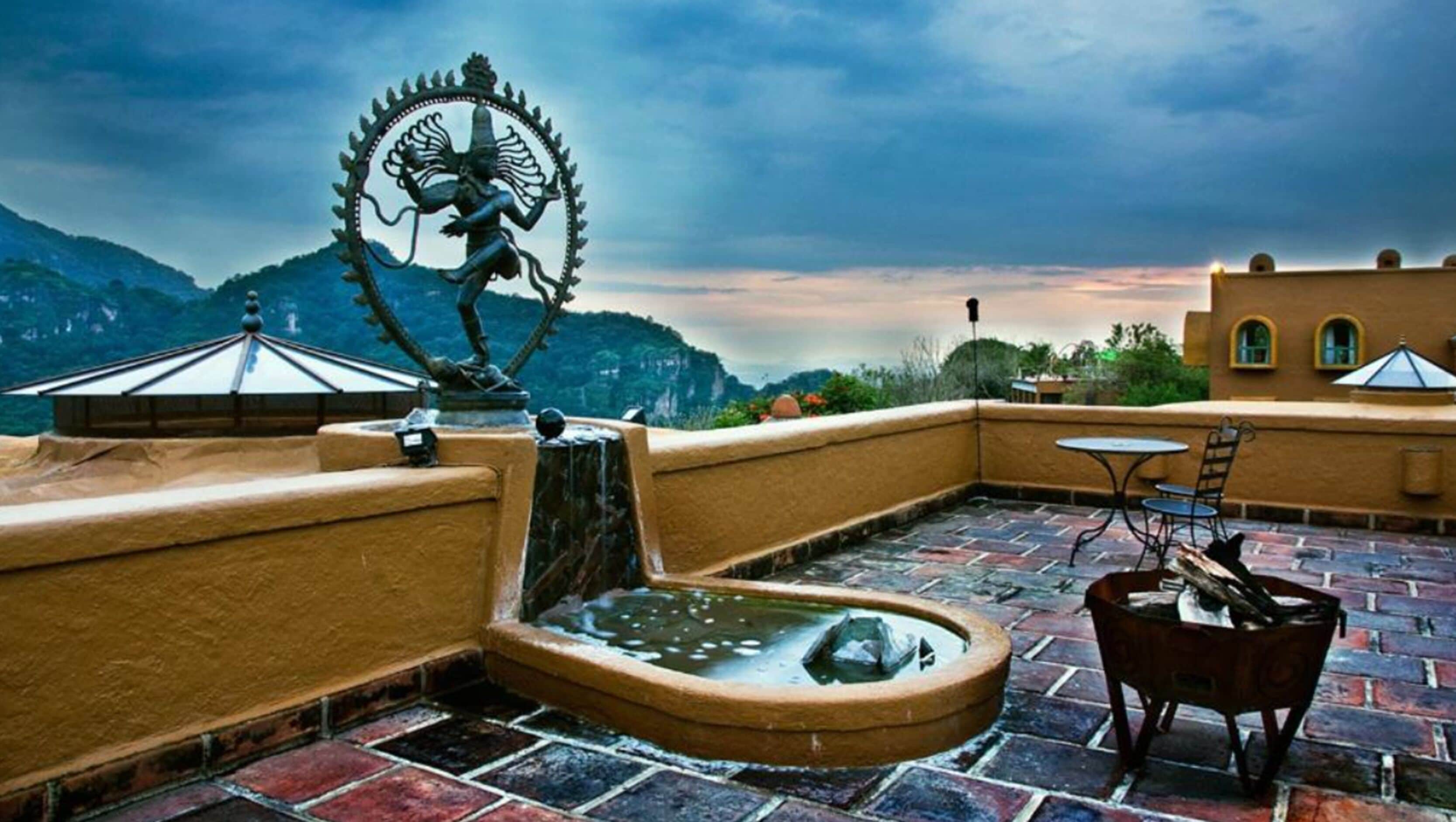 A rooftop terrace with a stone fountain, a statue, and a table with chairs.