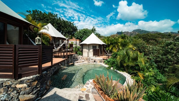 Una piscina con borde de piedra, terraza de madera y vista a un paisaje montañoso.