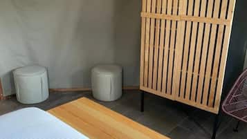 Un dormitorio con cama, un separador de madera, dos taburetes redondos y una alfombra colorida.