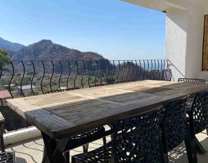 A wooden table with metal chairs on a balcony with a view of mountains. - Hostal de la Luz (Amatlán)
