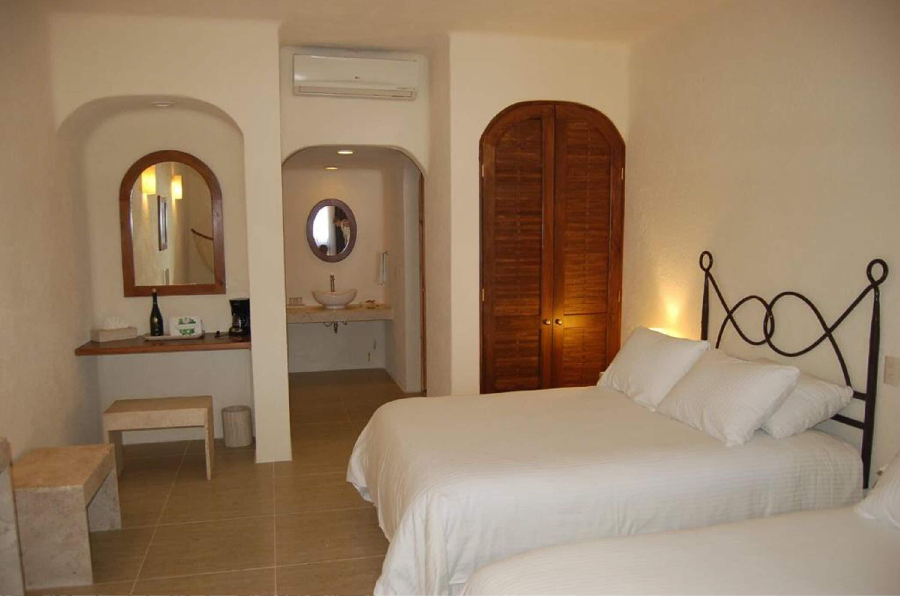 Une chambre avec deux lits, une armoire en bois, une coiffeuse avec un miroir et un banc.
