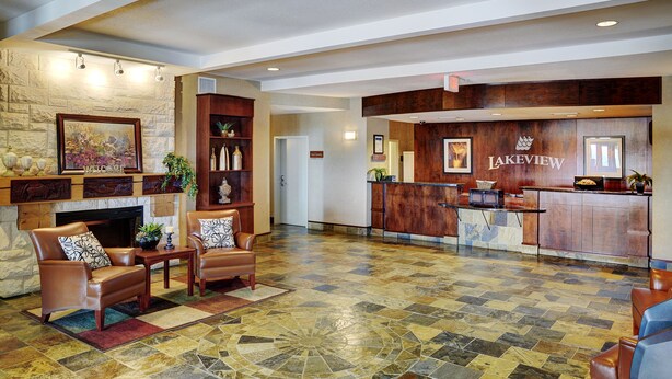 A lobby with a stone wall, a fireplace, leather chairs, a reception desk, and a "Lakeview" sign. - Lakeview Inns & Suites - Slave Lake (Slave Lake)