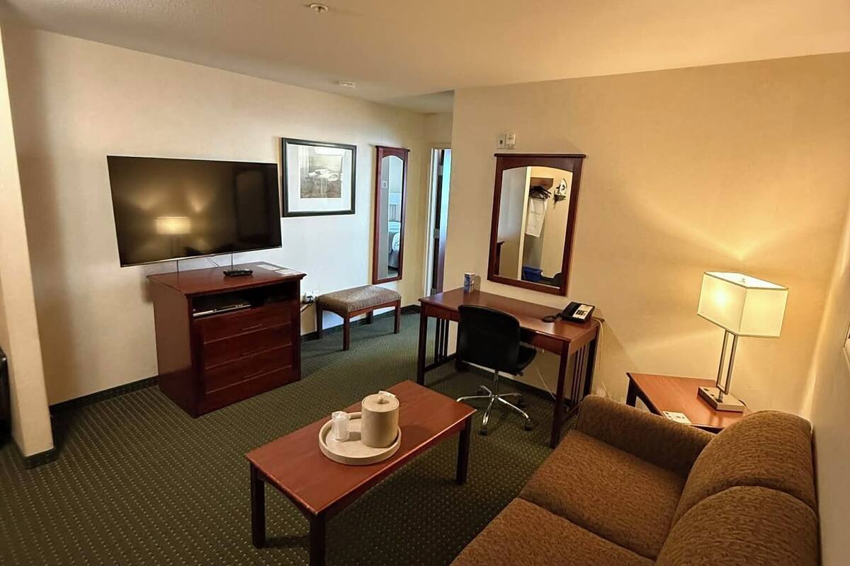 A hotel room with a flat-screen TV, a desk, a chair, a sofa, a dresser, and a mirror.