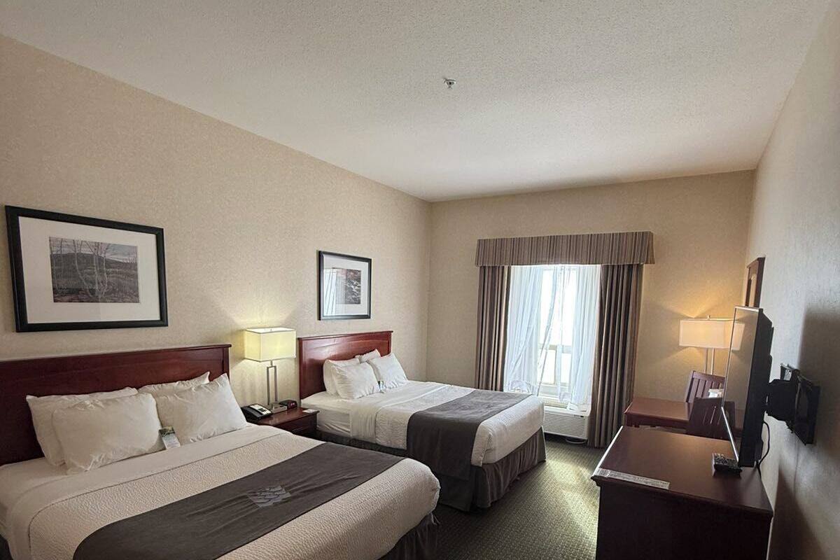 A hotel room with two beds, a desk, a chair, a lamp, and a window with curtains.