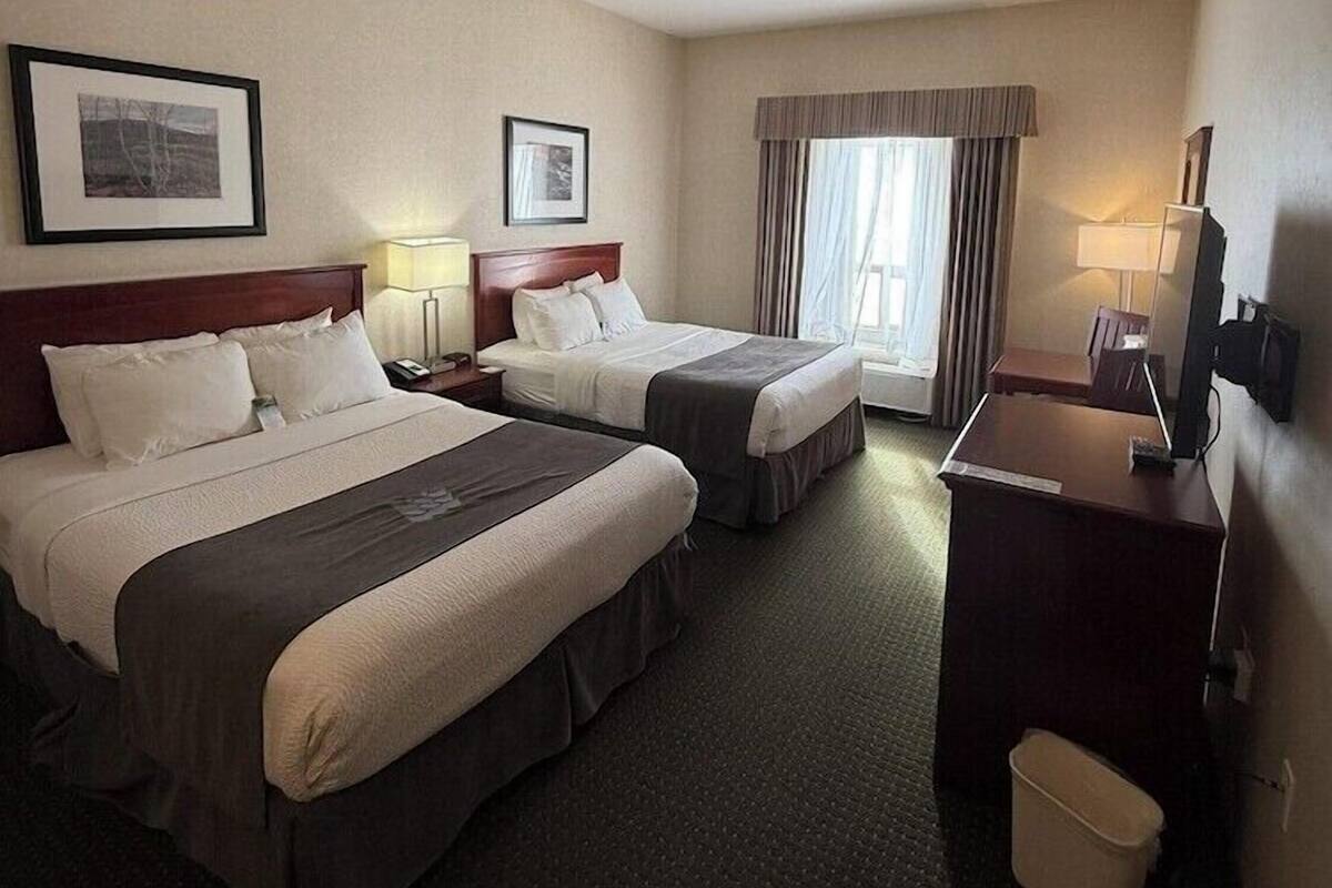 A hotel room with two beds, a desk, a chair, a TV, and a window with curtains.