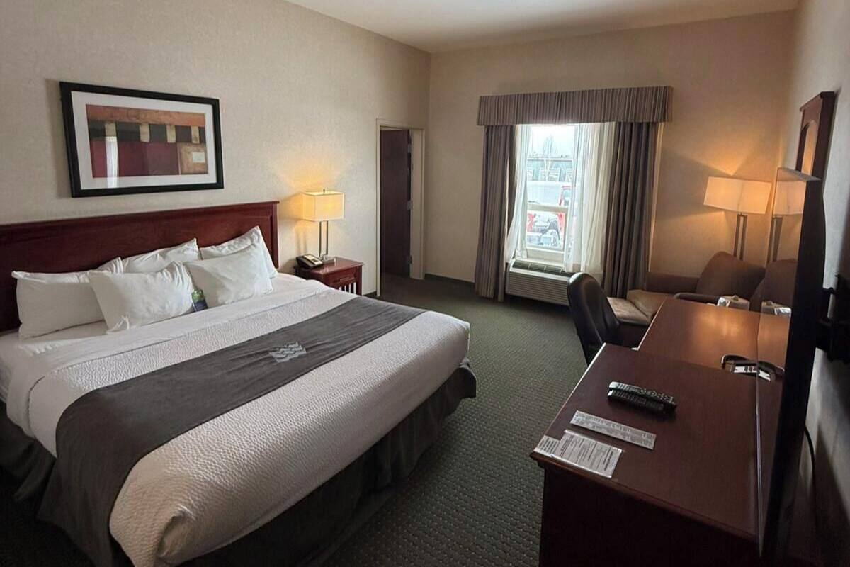 A hotel room with a large bed, a desk, two lamps, a framed picture on the wall, and a window with curtains.