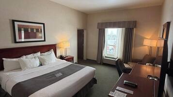 Habitación de hotel con una cama grande, un escritorio, dos lámparas, un cuadro enmarcado en la pared y una ventana con cortinas.