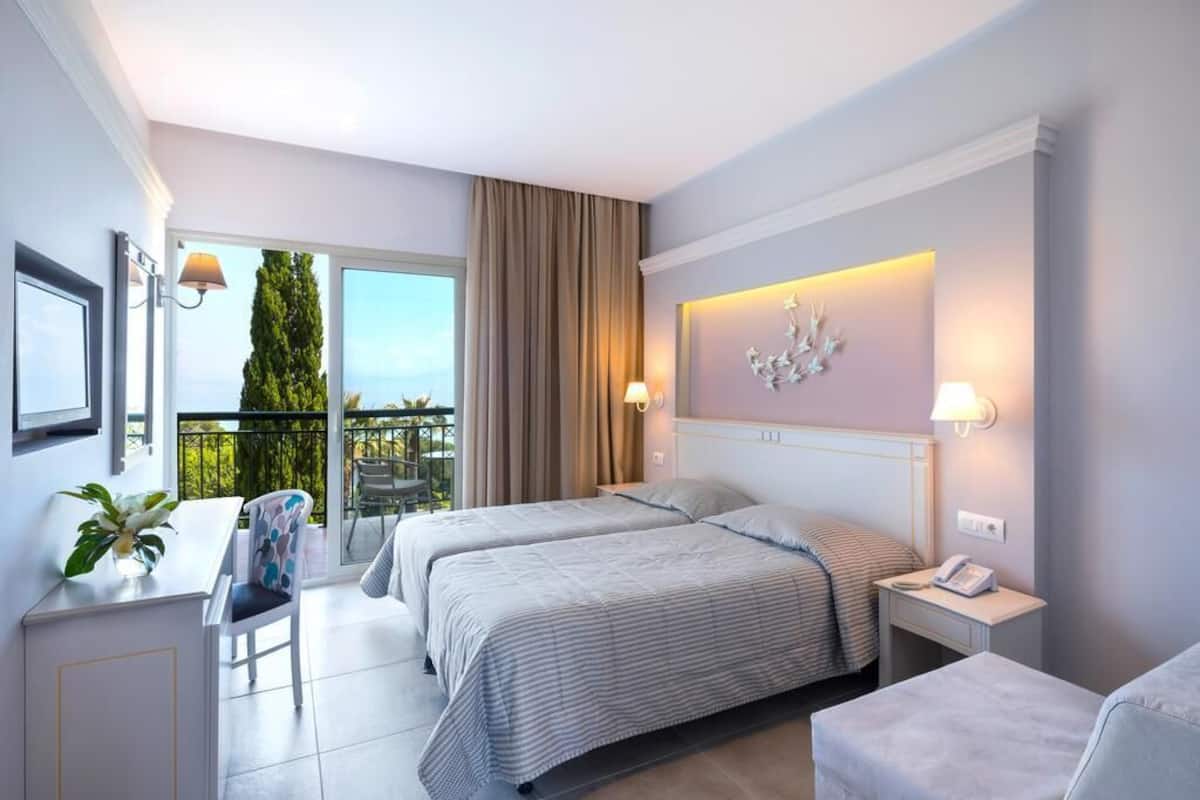 Habitación de hotel con dos camas, un escritorio, una silla, un balcón con vistas y un adorno en la pared.