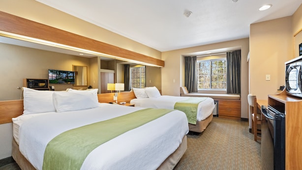 A hotel room with two beds, a desk, a microwave, a TV, and a window with curtains. - Parry Sound Inn & Suites (Parry Sound)