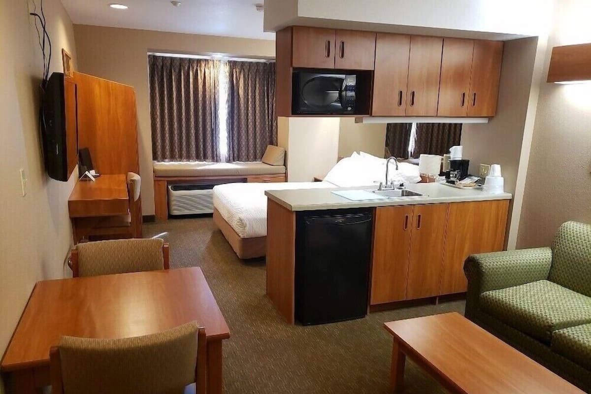 A compact hotel room with a kitchenette, a bed, a seating area, and a television.