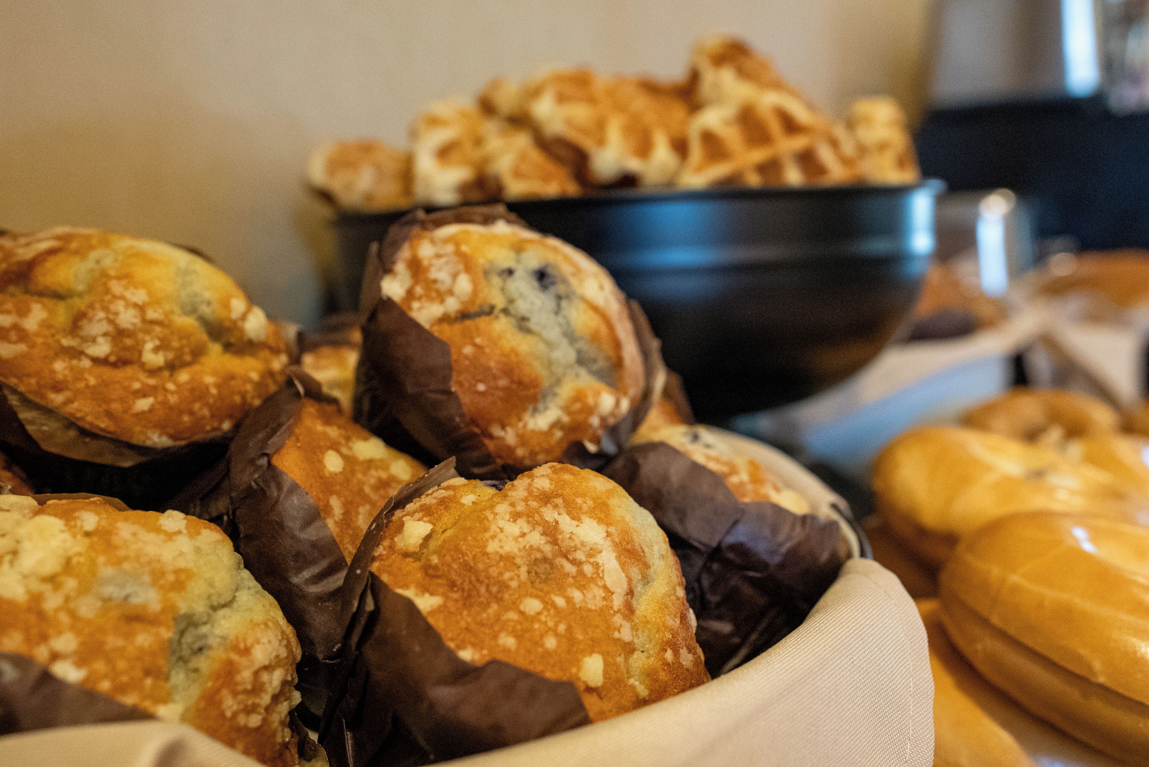 Variedad de productos horneados, como muffins y pan, expuestos en un bol y sobre una mesa.