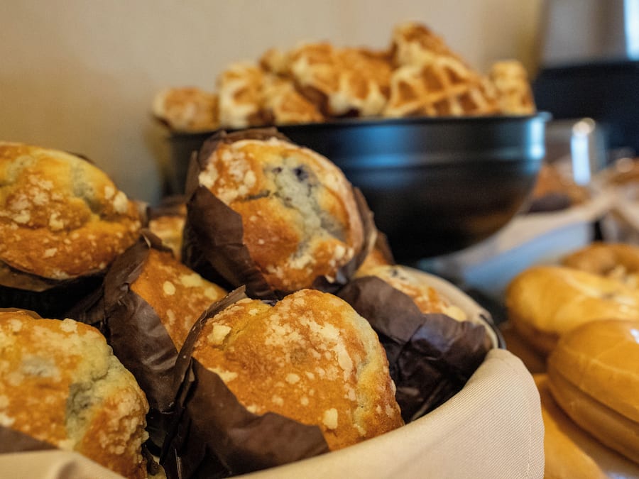 Variedad de productos horneados, como muffins y pan, expuestos en un bol y sobre una mesa.