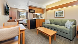 A compact living space with a kitchenette, a green sofa, a dining area, and a view of the outdoors. - Parry Sound Inn & Suites (Parry Sound)