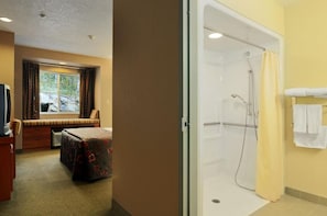 A hotel room with a bed, a television, a window with curtains, and a shower area with a towel rack. - Parry Sound Inn & Suites (Parry Sound)
