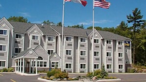 A multi-story hotel with a central entrance, two flags, and a parking lot. - Parry Sound Inn & Suites (Parry Sound)