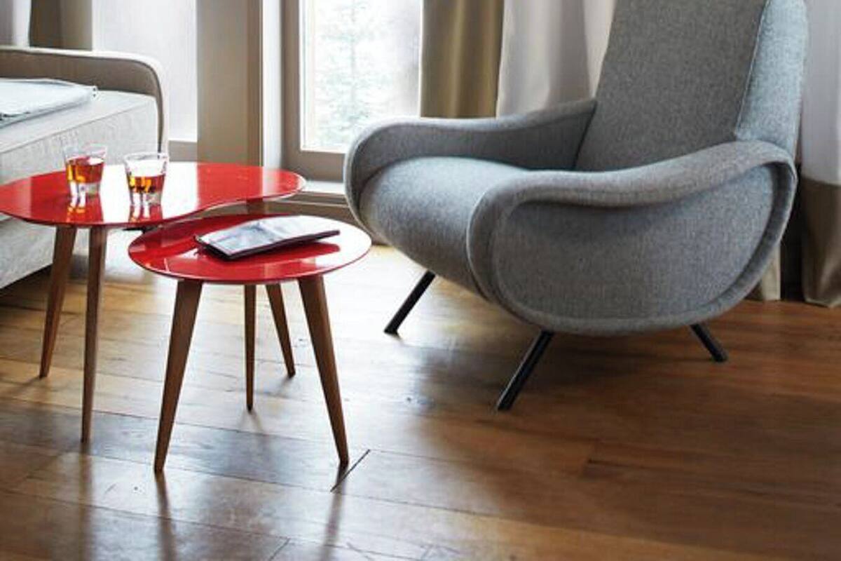 Una habitación moderna con un sillón gris, una pequeña mesa roja y un sofá blanco.