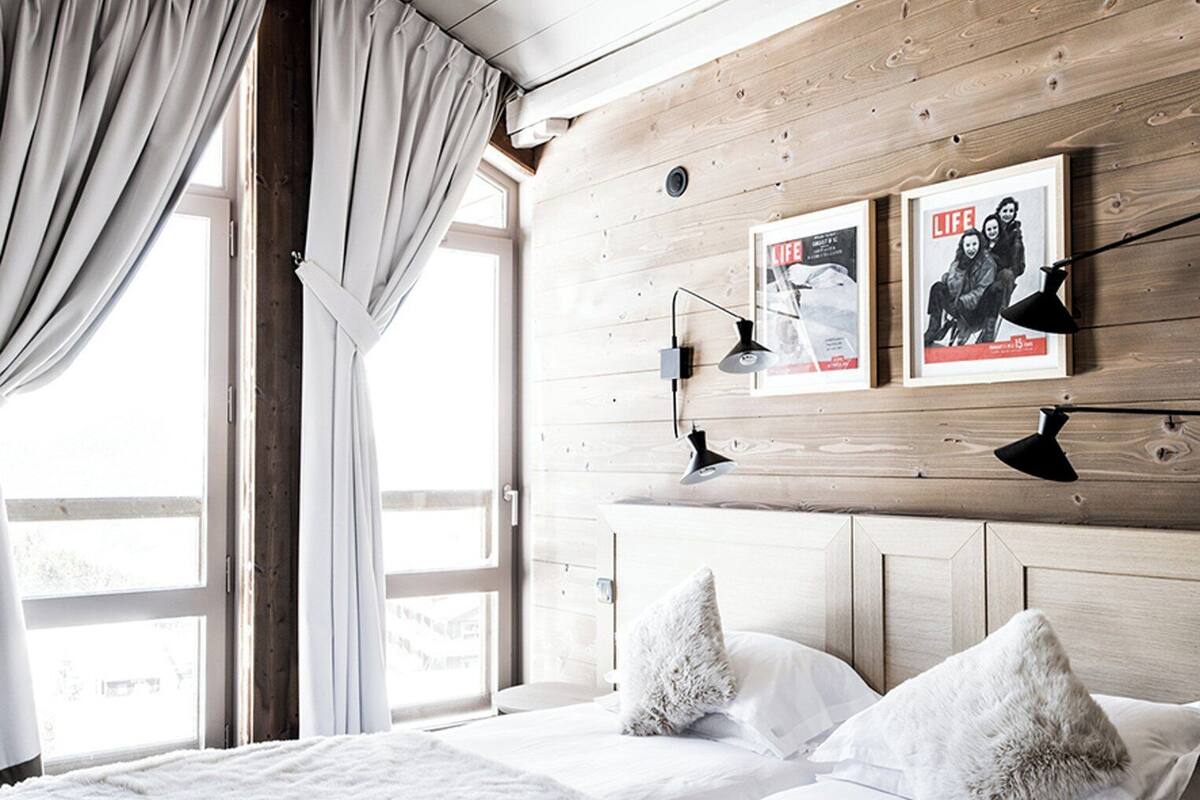 Un dormitorio con cabecera de madera, una cama grande con ropa blanca, dos almohadas mullidas y una ventana con cortinas.