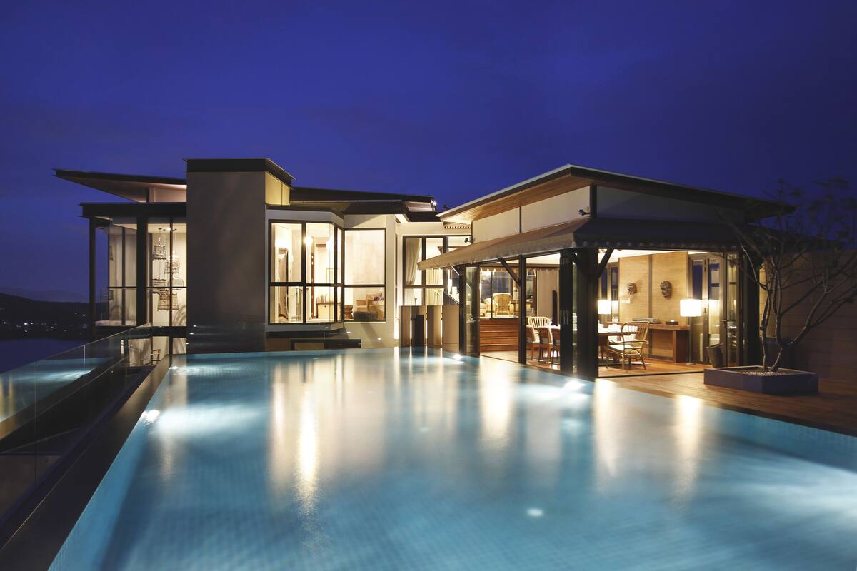 A modern house with a swimming pool, large windows, and a well-lit interior.