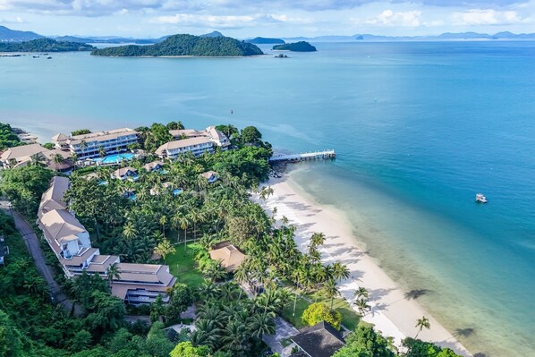 A resort with multiple buildings, a beach, and a pier extending into the ocean. - Cape Panwa Hotel (Wichit)