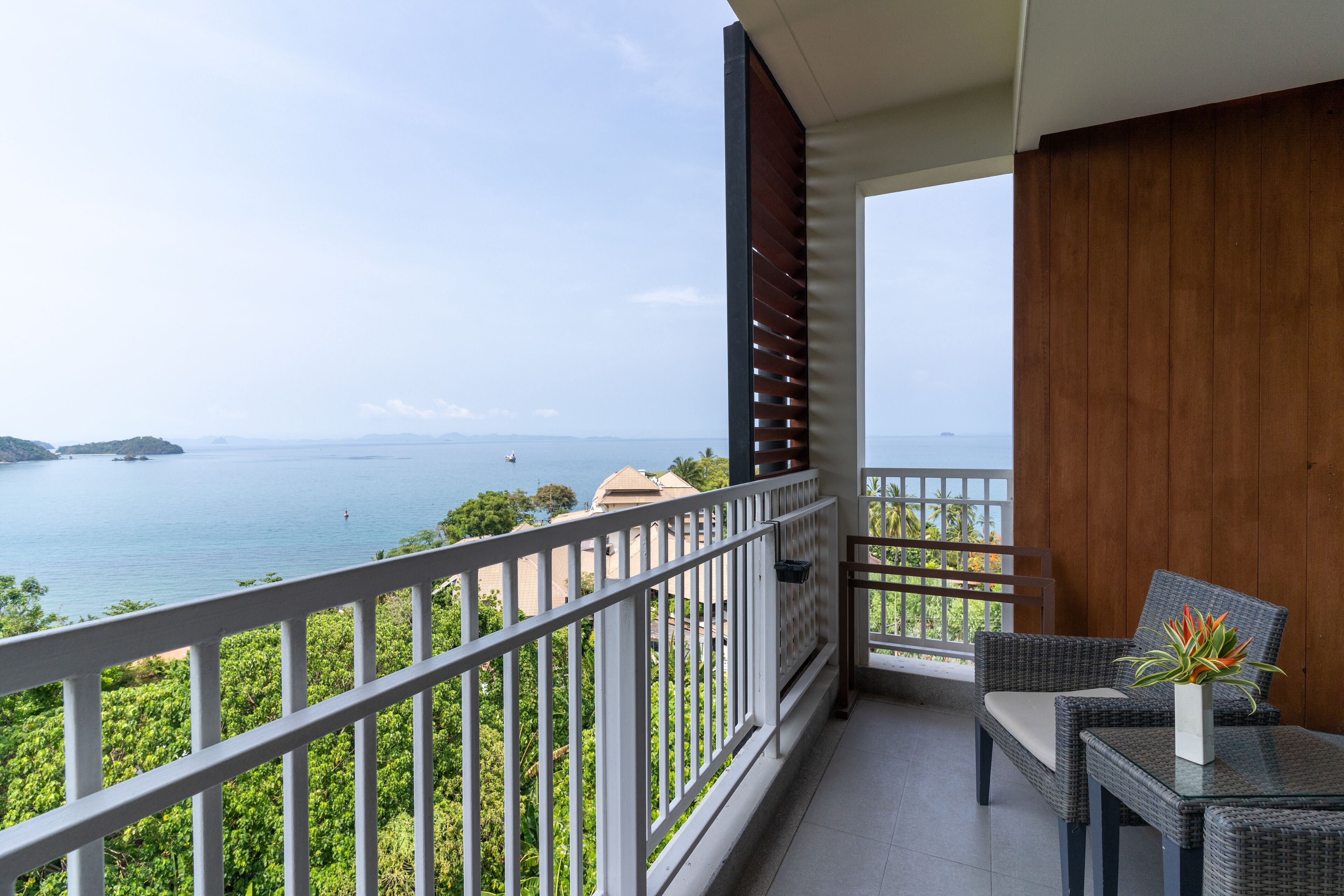 A balcony with a view of the sea, a wicker chair, a small table, and a potted plant.
