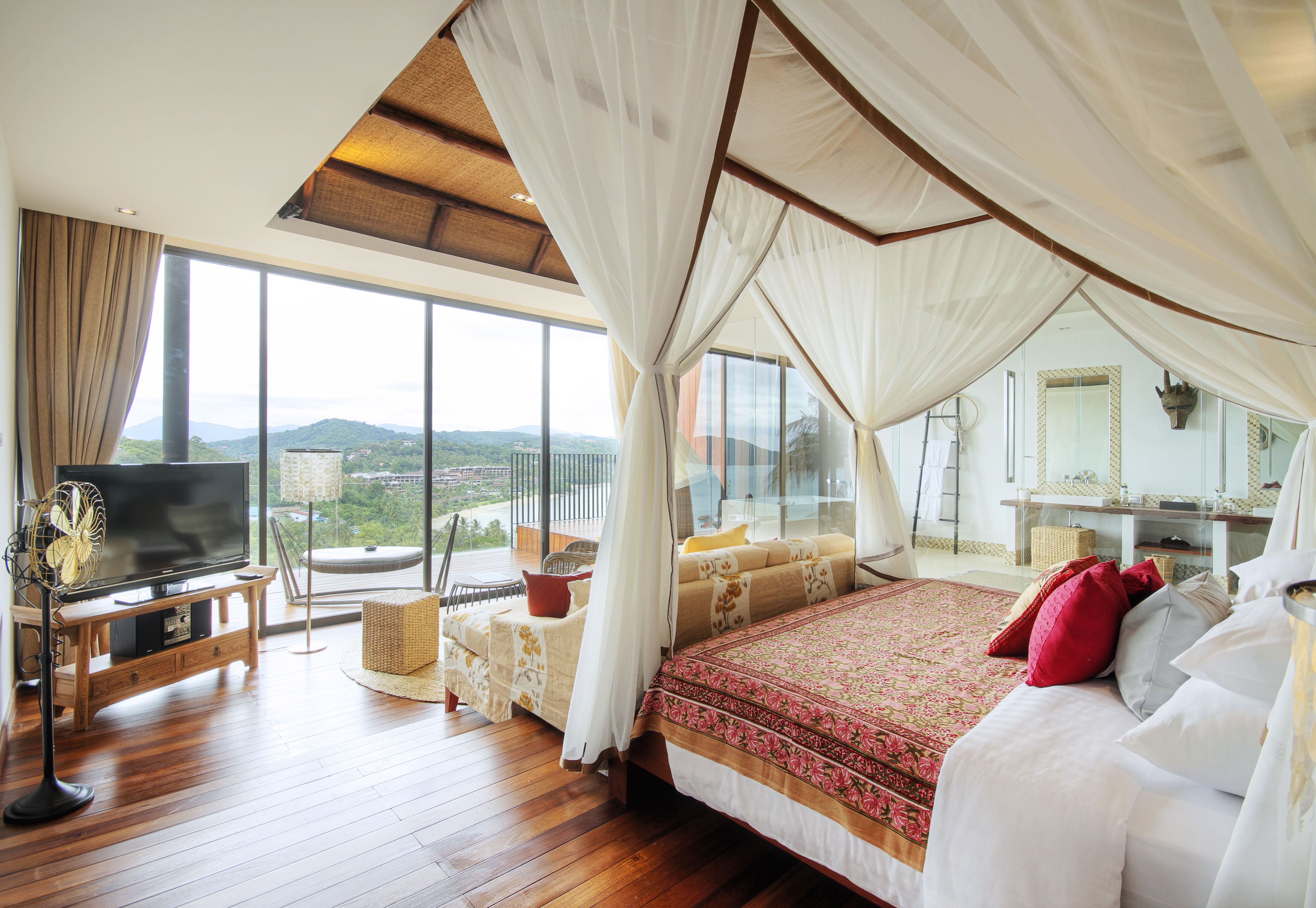 A spacious bedroom with a large bed, a television, and a balcony with a view of the mountains.
