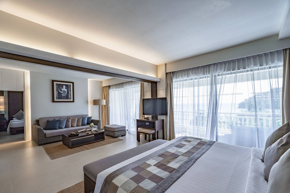 A modern hotel room with a large bed, a sofa, a desk, and a TV.