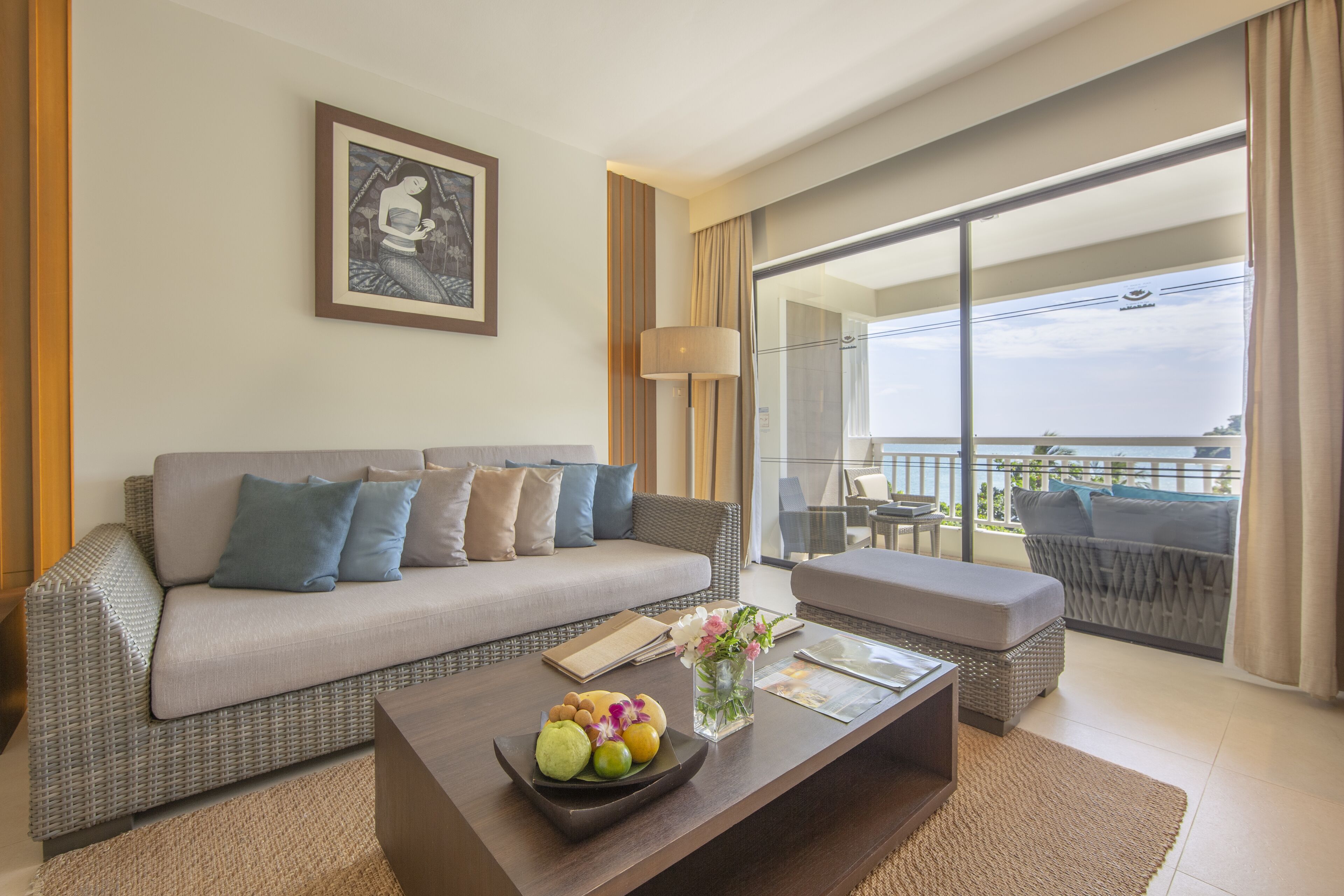A modern living room with a sofa, a coffee table with fruit, and a balcony with a view.