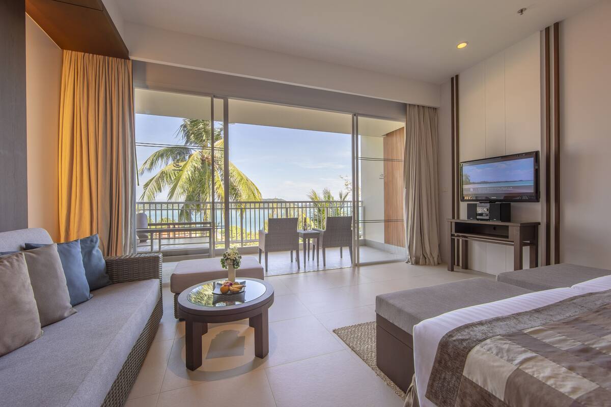 A hotel room with a balcony, a sofa, a bed, a TV, and a small table with fruit.