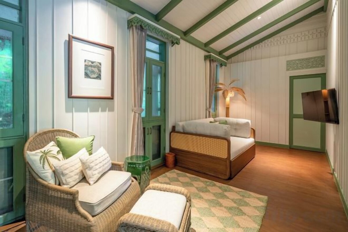 Quarto com cama, sofá de vime, mesa de cabeceira, quadro emoldurado e televisão.