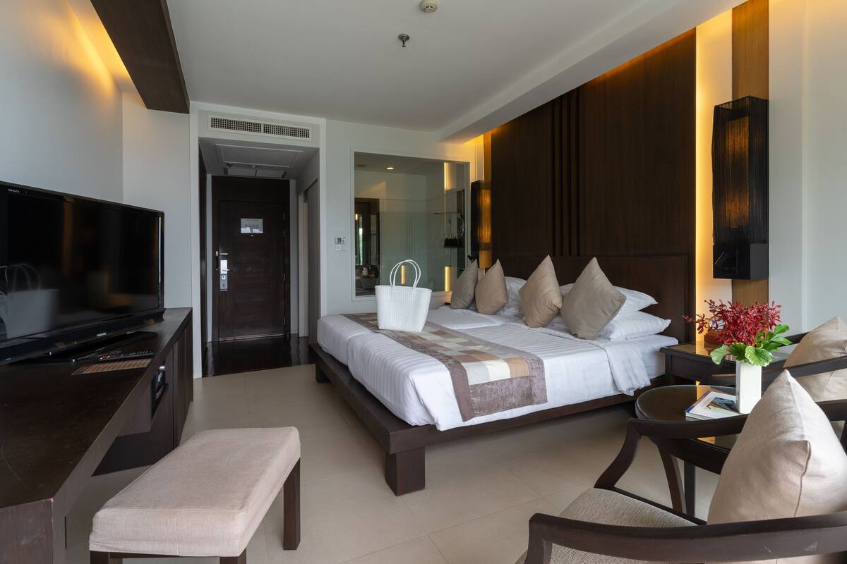 A modern hotel room with a large bed, a TV, a desk, and a seating area.
