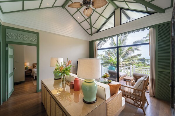 A room with a balcony, a bed, a desk with a lamp, and a view of palm trees.