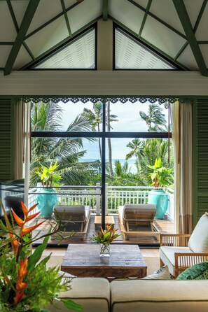 A balcony with a view of palm trees and the ocean, furnished with a sofa, chairs, and a coffee table. - Cape Panwa Hotel (Wichit)