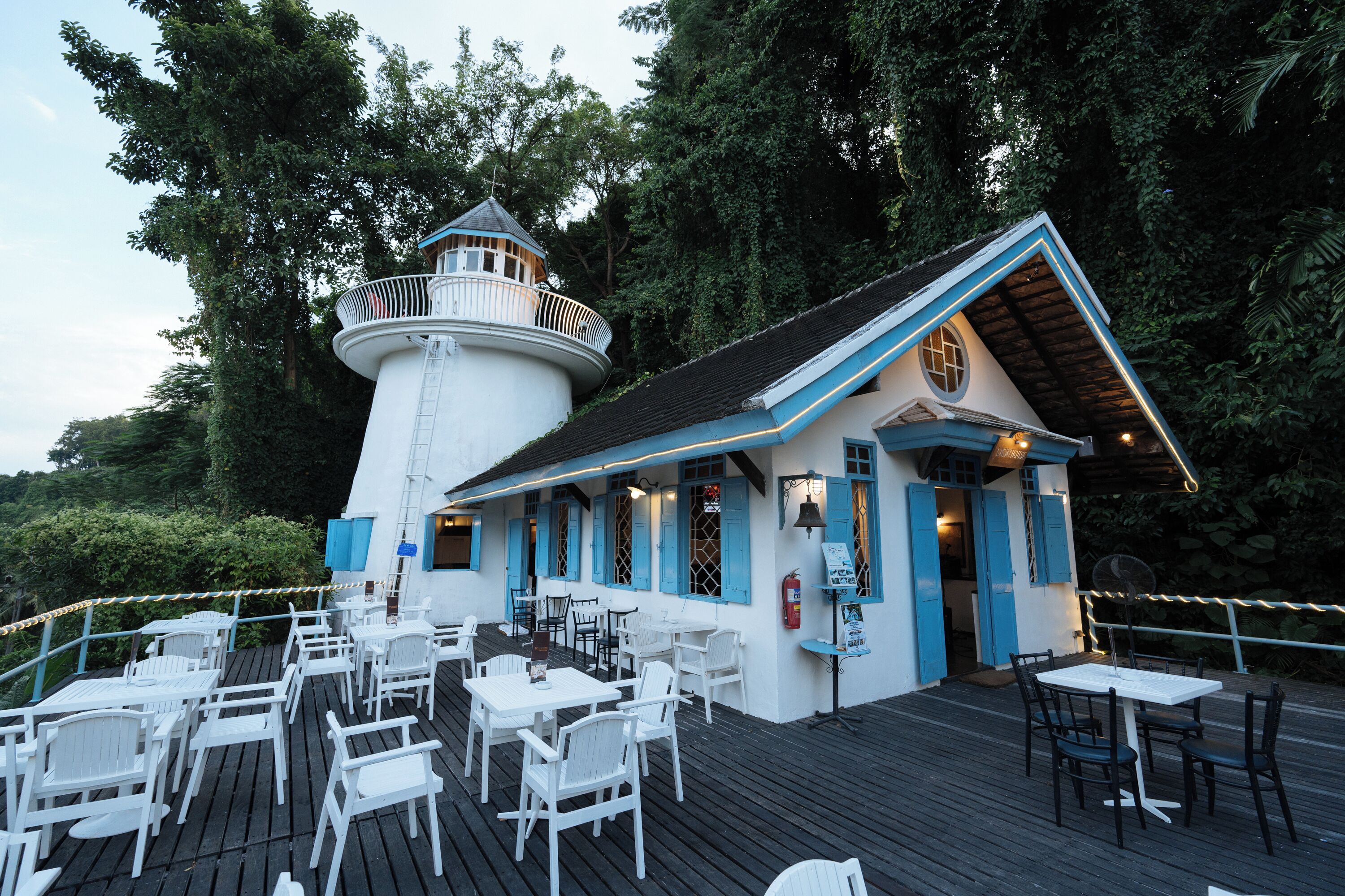 A lighthouse with a balcony and a dining area with white chairs and tables.