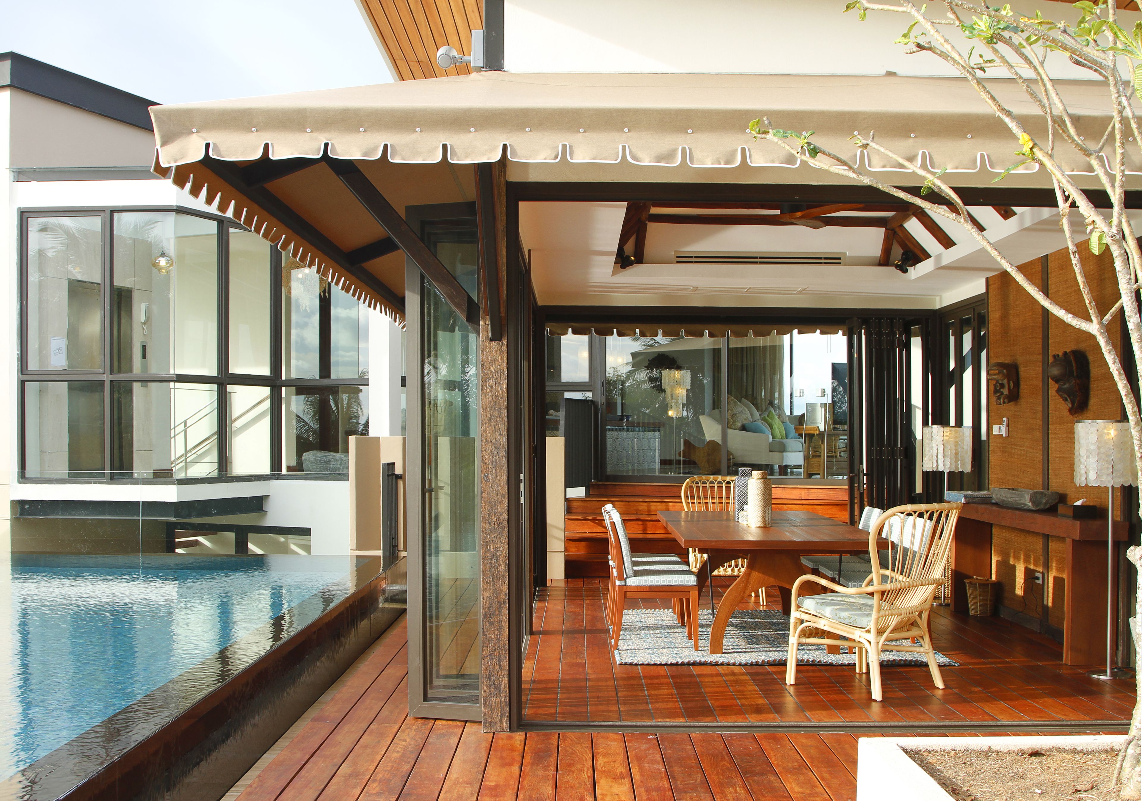 Un espacio moderno para comer al aire libre con piscina, piso de madera y puertas de vidrio que dan al interior.