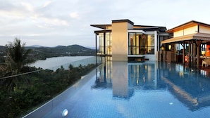 A modern infinity pool with a clear view of a lake and mountains, surrounded by lush greenery.
