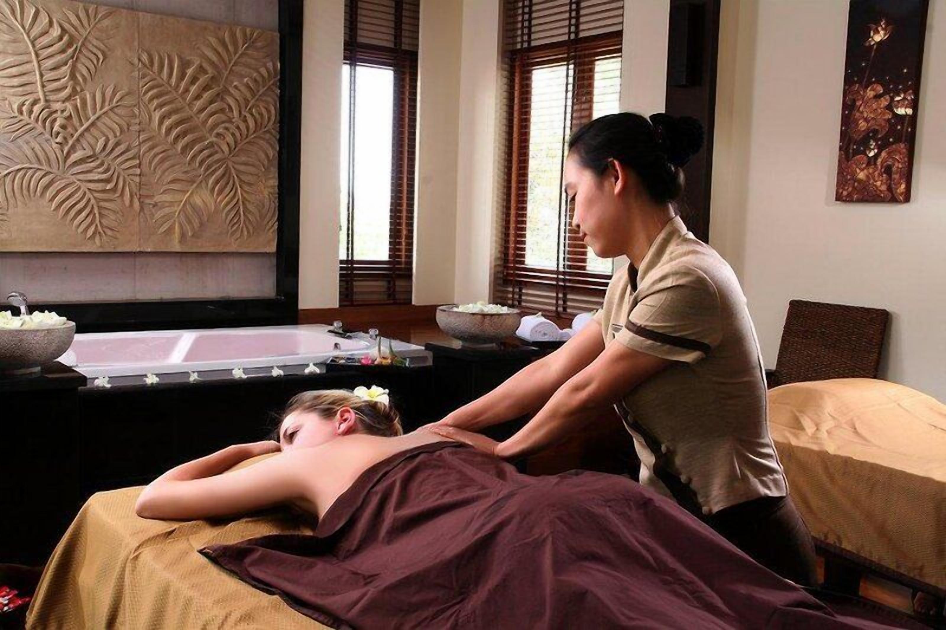 A massage therapy room with a massage table, a massage therapist, and a decorative wall.