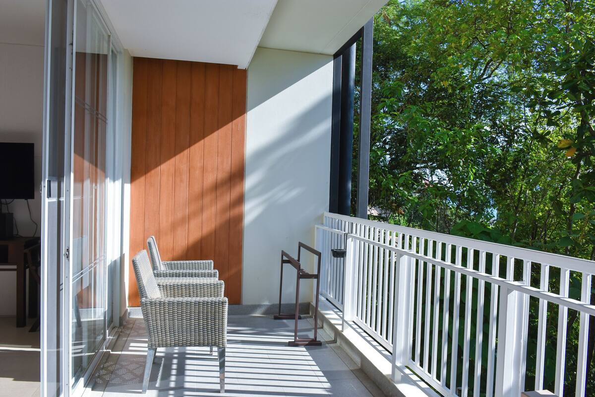 A balcony with wicker chairs, a small table, and a wooden panel wall.